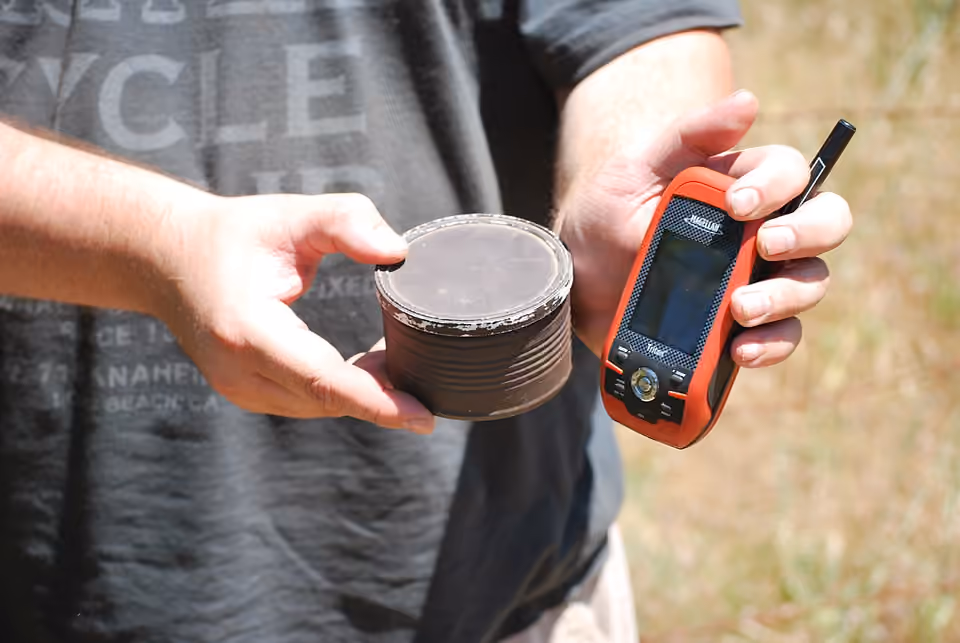 Une petite boîte de géocache accompagnée d’un récepteur GPS.