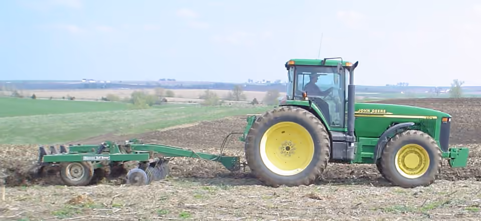 Un tracteur travaille le sol avec un outil à dents.