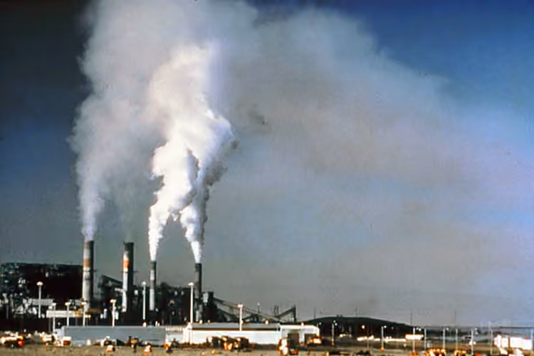 Vue historique d’un site industriel avec des cheminées et des panaches dans le ciel.