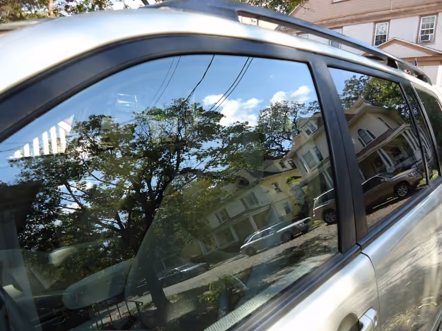 Végétation et bâtiments reflétés dans la vitre d’une voiture.