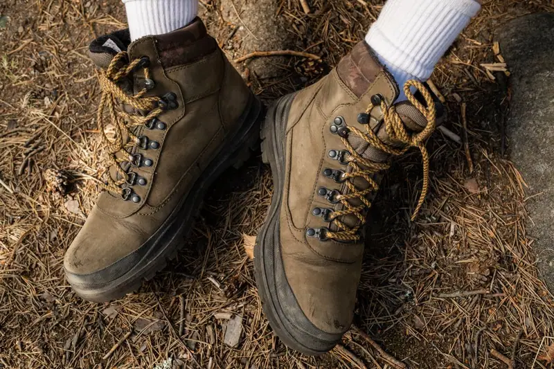 Gros plan sur des chaussures de randonnée brunes portées sur un sol forestier.