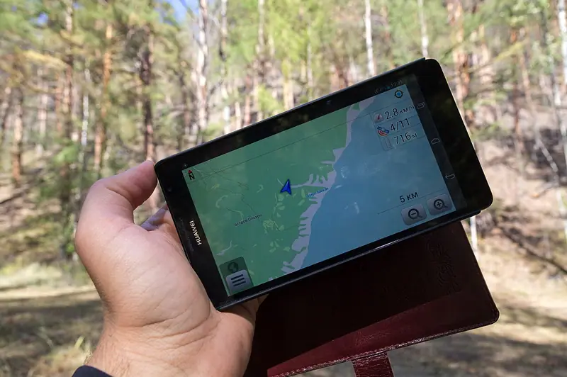 Une main tient un téléphone affichant une carte de navigation devant un sentier boisé.