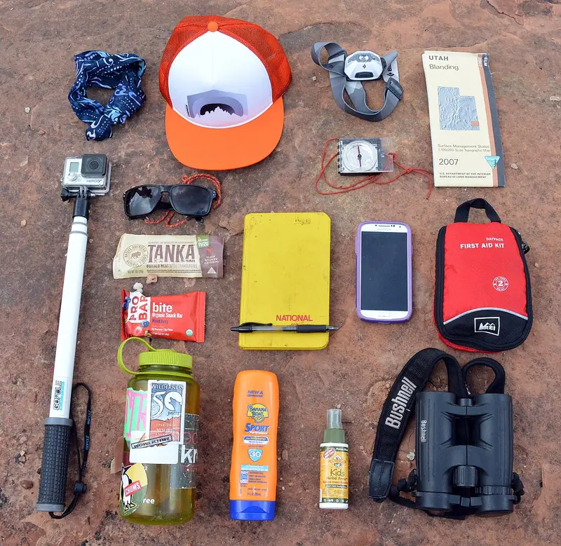 Matériel de randonnée disposé au sol, avec une carte, une boussole, un téléphone et une trousse.